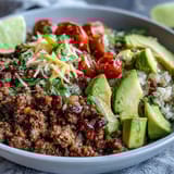 A close-up of a Low Carb Burrito Bowl with juicy tomatoes, shredded cheddar, and a dollop of sour cream on a rustic table.