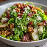 A close-up of the Frisée Pear Blue Cheese Bowl showing toasted walnuts and zesty vinaigrette drizzled over the vibrant salad greens.