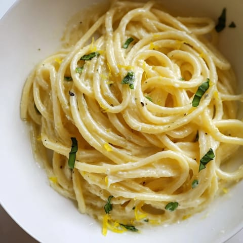 A close-up shows creamy lemon ricotta pasta in a white bowl, topped with fresh herbs and black pepper.