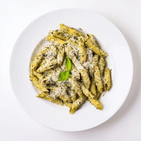 A close-up of creamy sunflower seed pesto pasta twirled on a fork, showcasing vibrant green sauce and fresh basil garnish.  