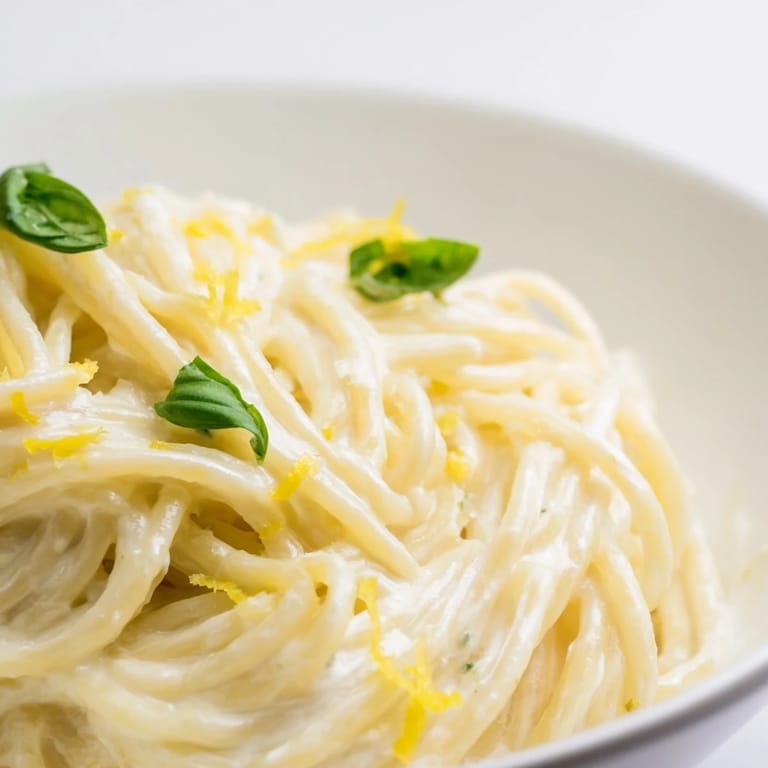 Delicious lemon ricotta pasta served in a shallow bowl with a glass of white wine on a rustic table.