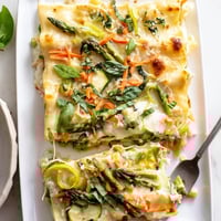 Baked Spring Veggie Alfredo Lasagna with golden, bubbly mozzarella topping and fresh basil garnish.